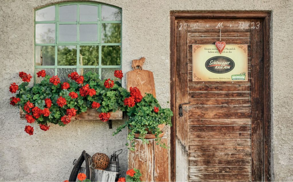 Der gemütliche Eingang des Hofladensmit roten Blumen und einer Holtzüre
