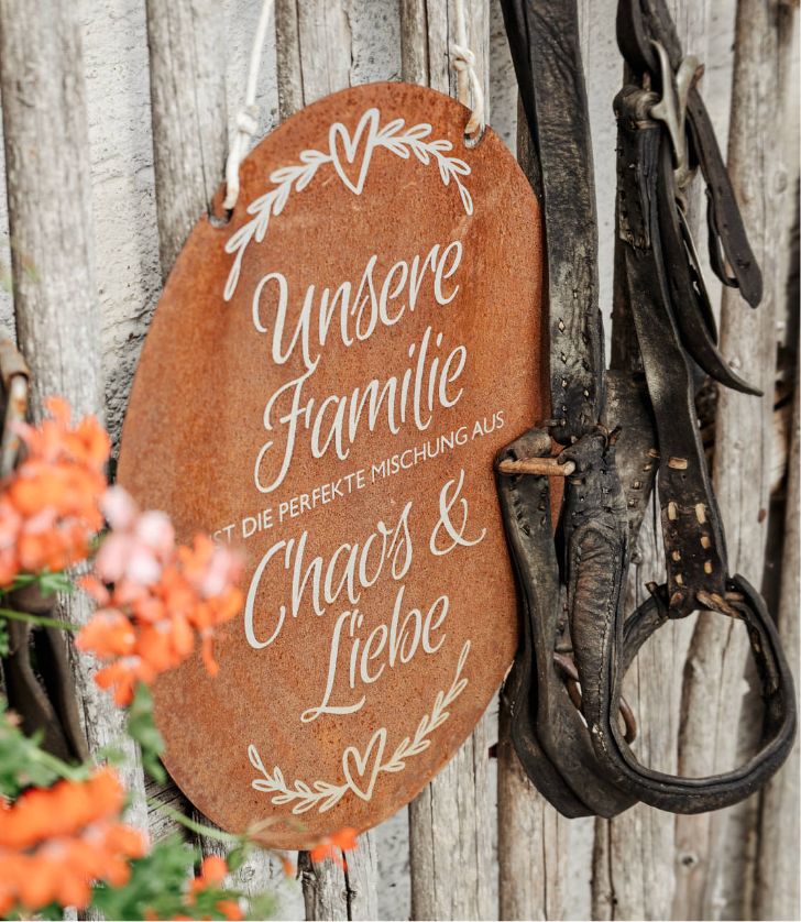 Ein Schild aus Rost am Zaun mit einem schönen Schriftzug "Unsere Familie ist die perfekte Mischung aus Chaos & Liebe"