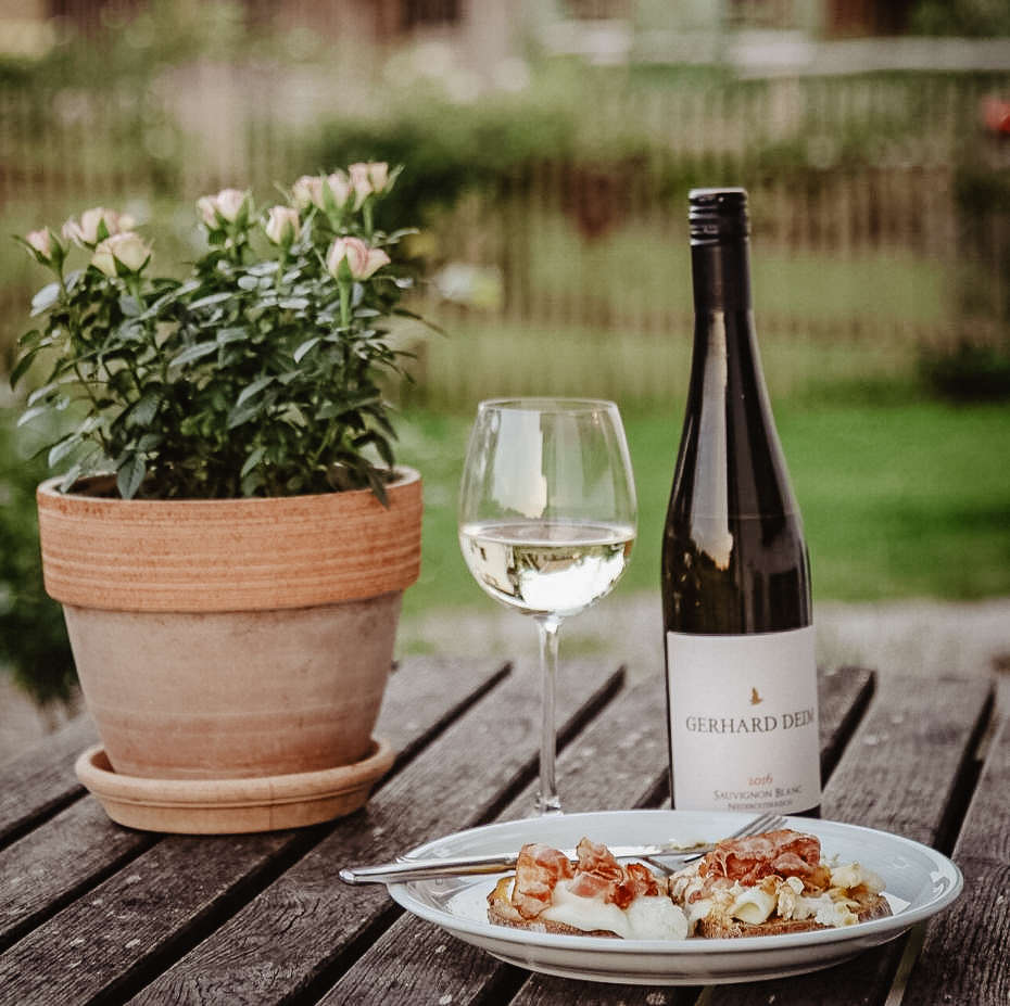 Ein Brotzeitteller mit einem Glas Wein und einer Weinflasche auf dem Tisch im Garten