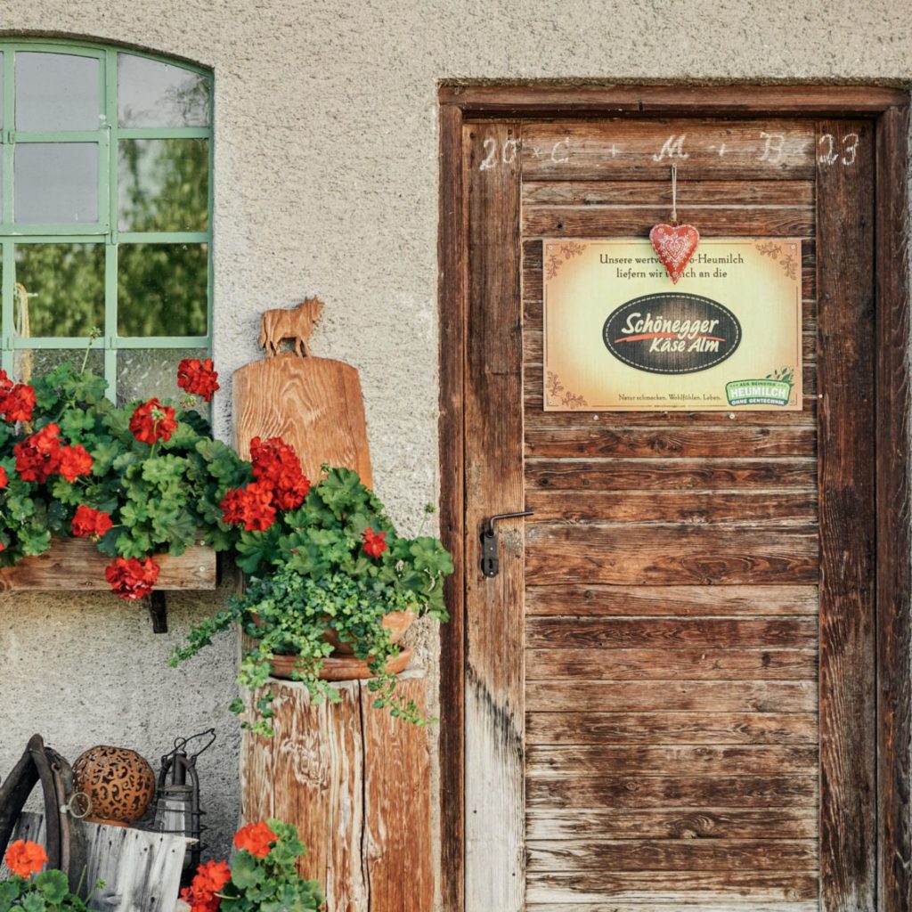 Der gemütliche Eingang des Hofladensmit roten Blumen und einer Holtzüre